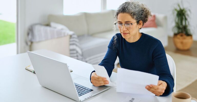 Signora che seduta al tavolo confronta una fattura con uno scontrino mentre è davanti al PC