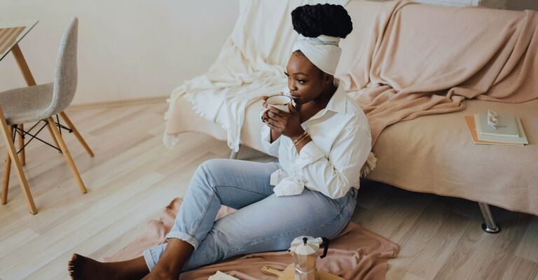 Donna seduta per terra che beve un caffè dalla moka mentre sembra riflessiva