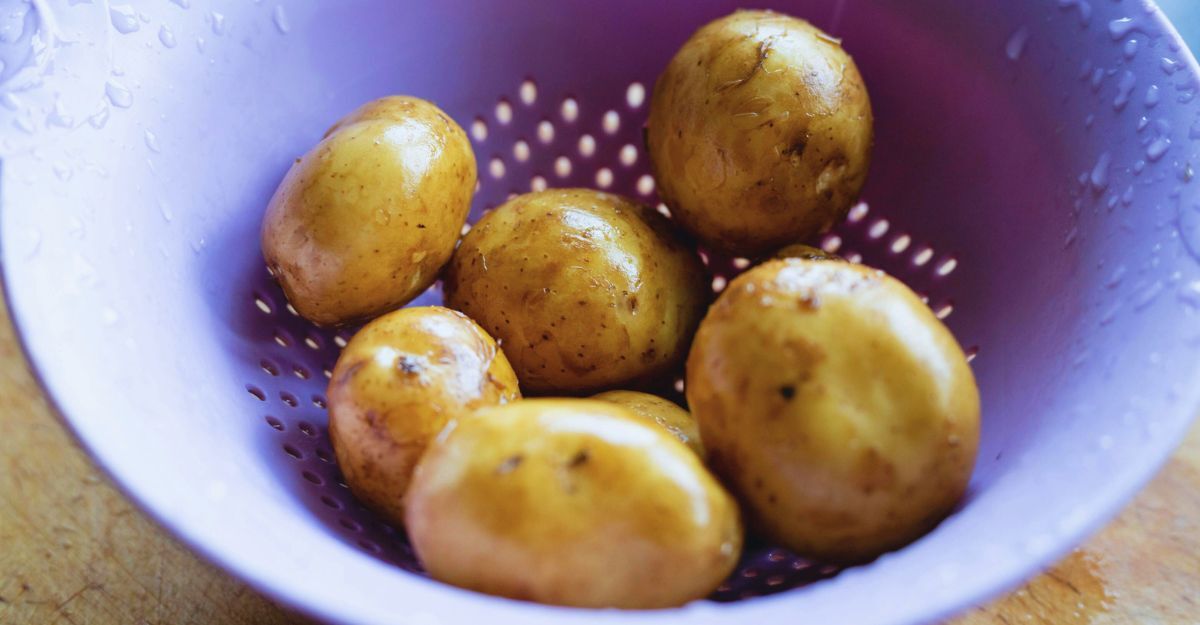 Scolapasta lilla con all'interno patate lavate con la buccia