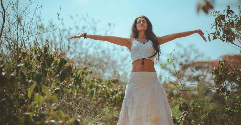 Donna in piedi con braccia spalancate e occhi chiusi e vestita in stile boho