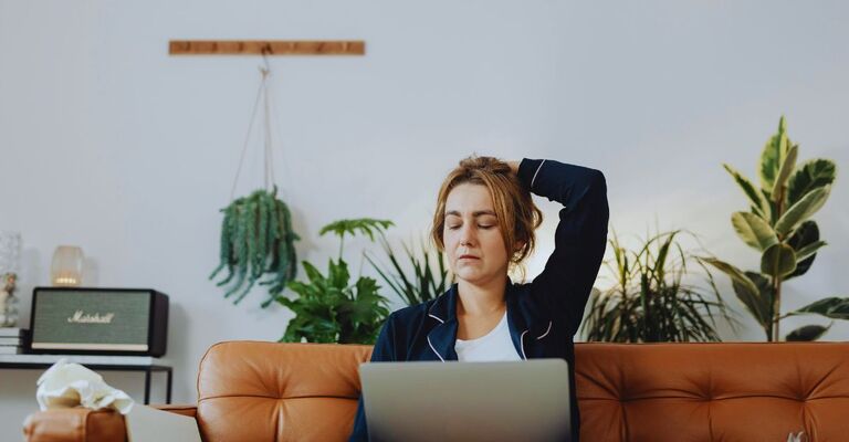 Donna stanca con braccio dietro la testa e occhi chiusi seduta sul divano con il PC sulle gambe