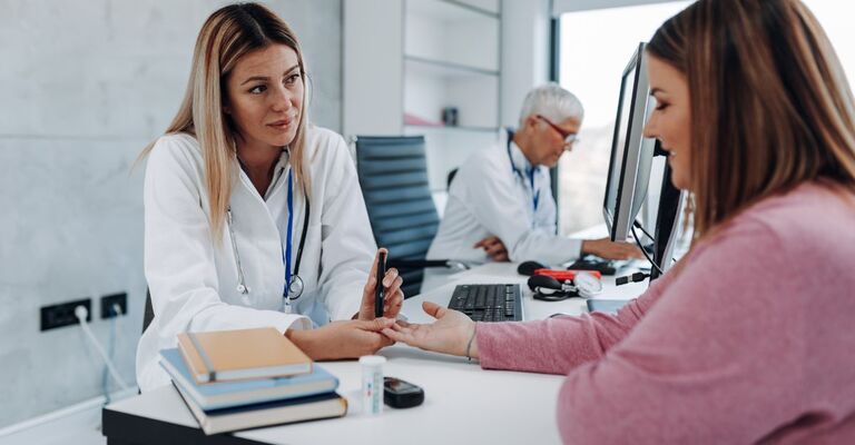 Dottoressa in uno studio medico che misura la glicemia a una sua paziente seduta di fronte a lei