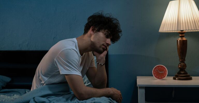 Un ragazzo seduto sul letto che non riesce a dormire bene la notte