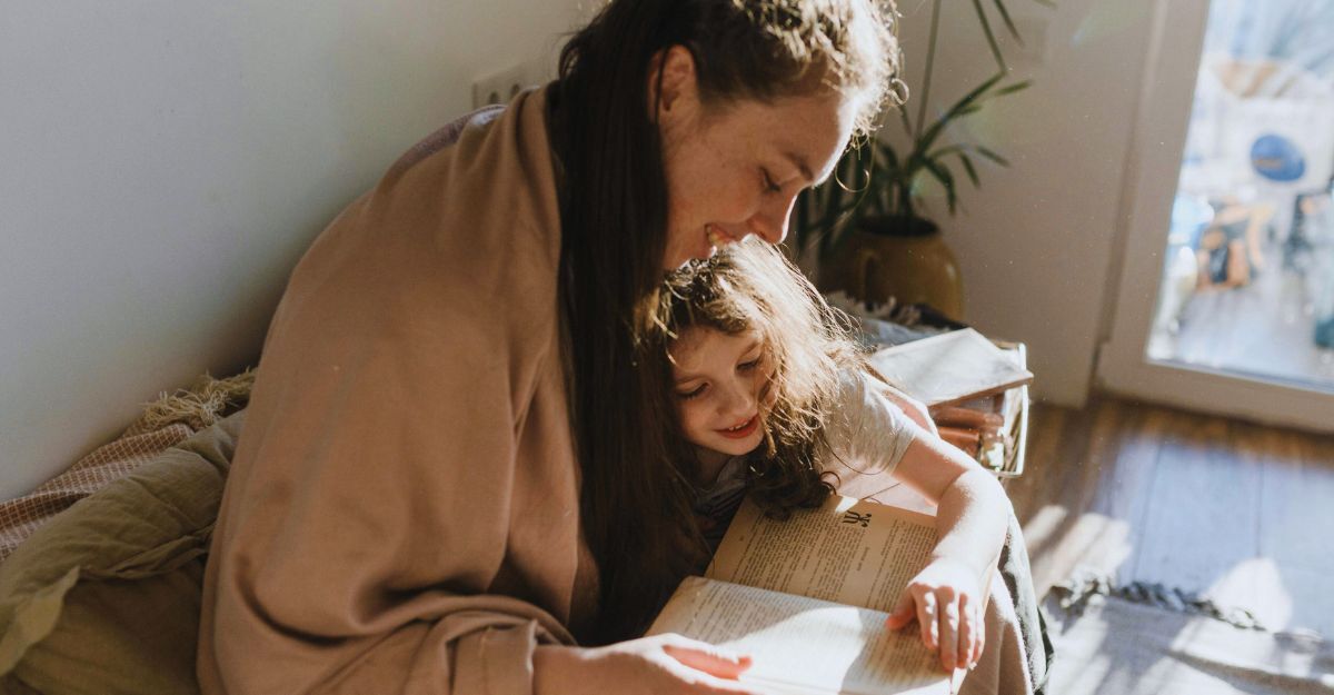 Mamma che legge con sua figlia sedute sul divano mentre sorridono
