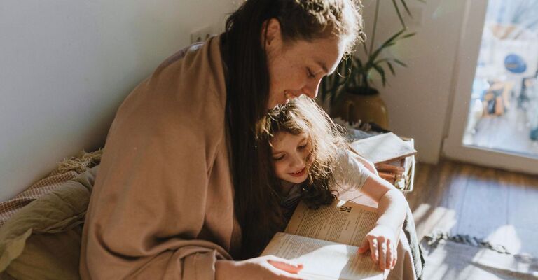 Mamma che legge con sua figlia sedute sul divano mentre sorridono