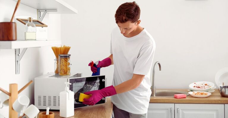 Ragazzo che pulisce il microonde in cucina con dei guanti bordeaux