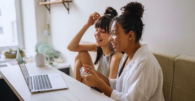 Due ragazza che giocano insieme a un gioco al PC utilizzando un joystick mentre ridono