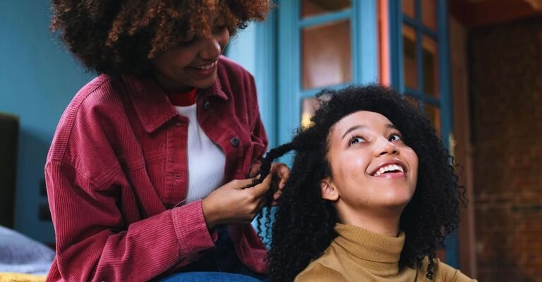 Due sorelle che sorridono insieme mentre una sistema i capelli afro all'altra