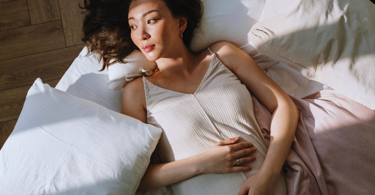 Donna incinta preoccupata che si tocca il ventre mentre è sdraiata sul letto