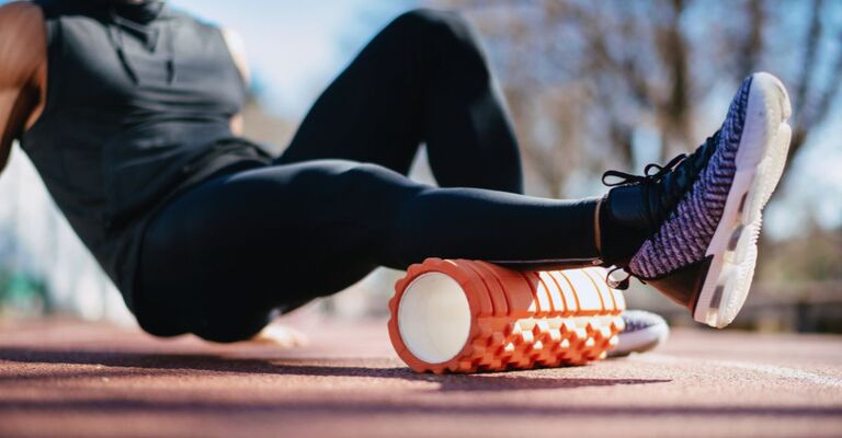 Uomo che ha appena corso fa stretching con il foam roller sulla pista da corsa per i polpacci