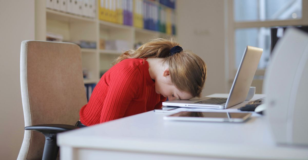 Giovane ragazza seduta alla scrivania con la testa poggiata sul PC e gli occhi chiusi