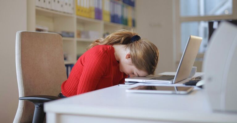 Giovane ragazza seduta alla scrivania con la testa poggiata sul PC e gli occhi chiusi