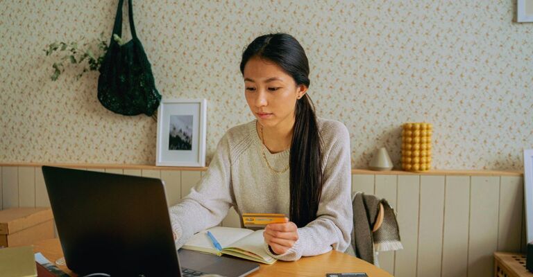 Ragazza in casa davanti al PC con la carta di credito in mano che valuta un acquisto
