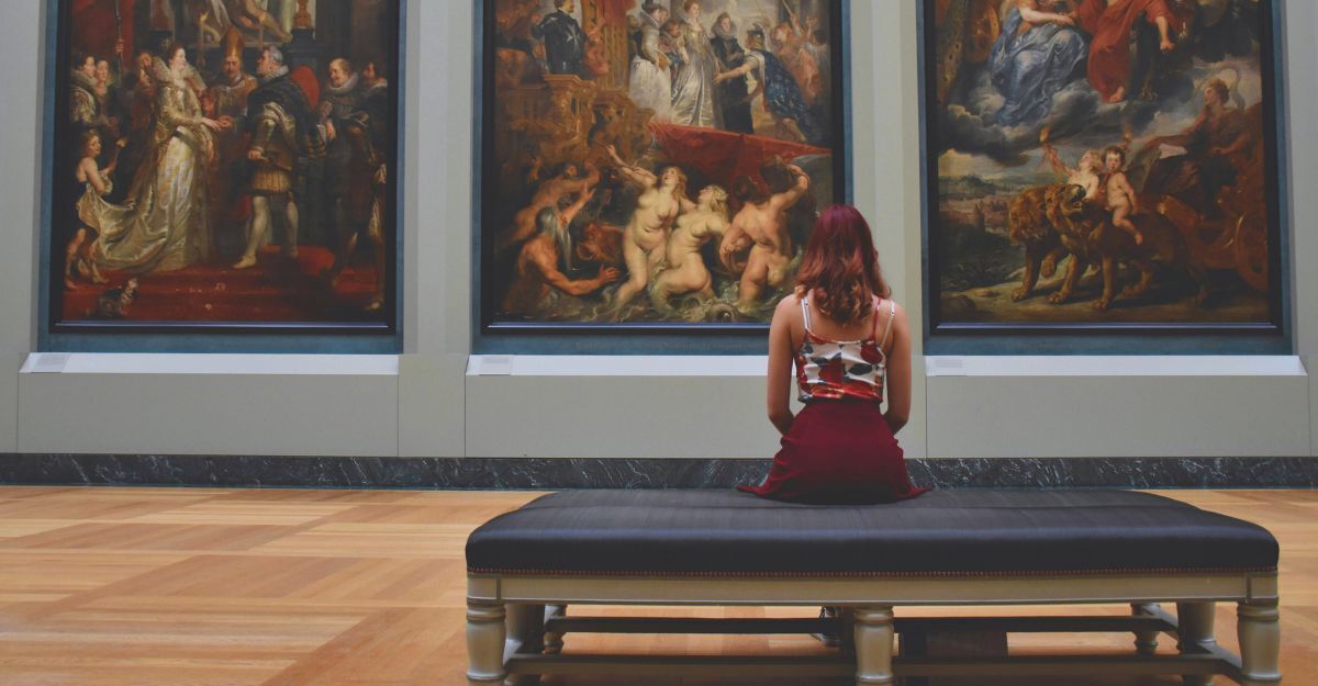 Donna seduta su una panca di un museo di fronte a tre quadri