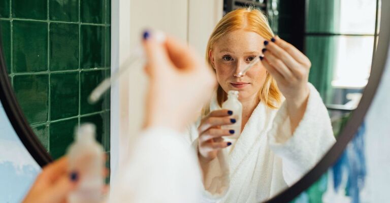 Ragazza davanti allo specchio che dosa il siero con la pipetta in accappatoio