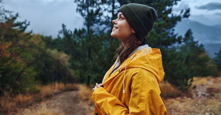Ragazza con impermeabile giallo e cappellino che guarda in alto sorridendo in una foresta