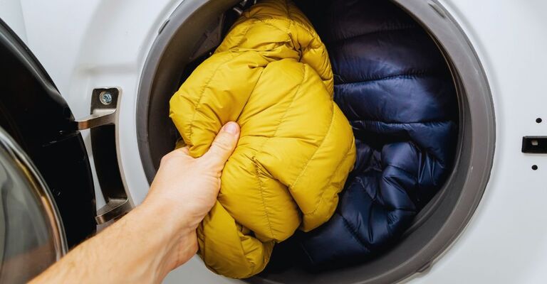 Mano che inserisce dei piumini dentro il cestello della lavatrice