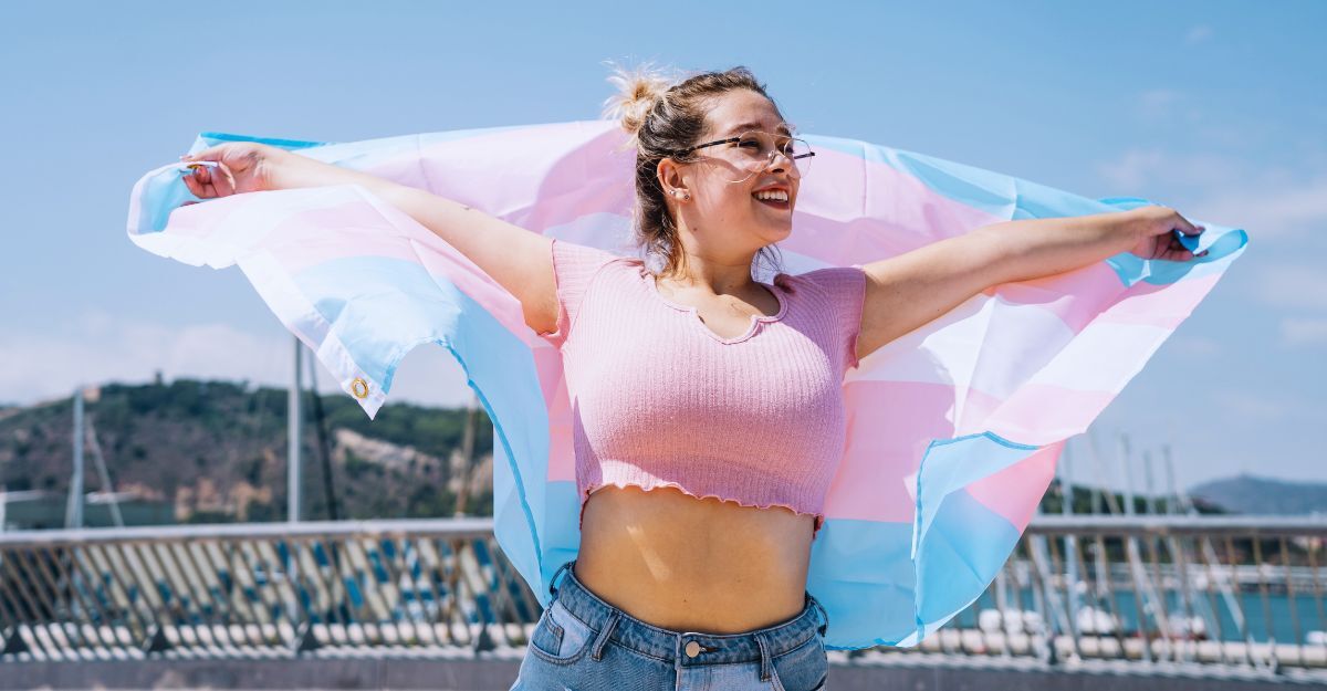 Donna trans che tiene la bandiera della comunità trans alle sue spalle