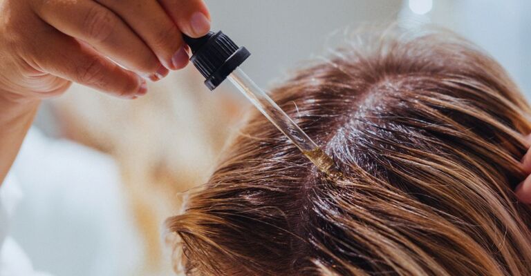 Mano con una pipetta che distribuisce dell'olio sul cuoio capelluto
