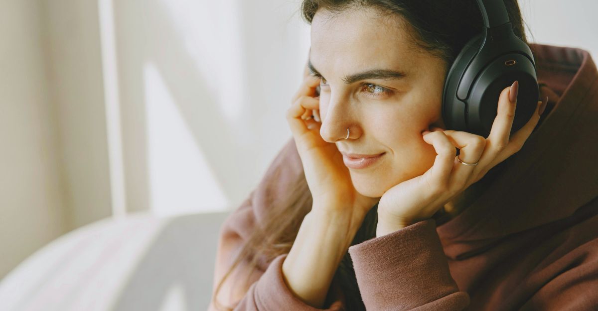 Ragazza che guarda fuori dalla finestra e ascolta musica con le cuffie sulle orecchie