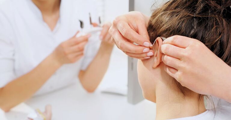 Due audiometriste aiutano una paziente a inserire un apparecchio acustico