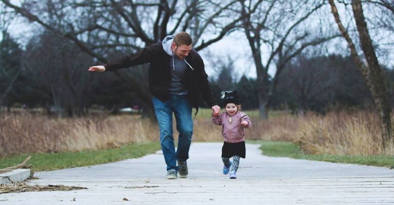 Un papà e una bambina piccola mano nella mano che corrono insieme in un parco