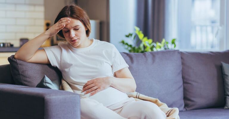 Donna incinta seduta sul divano e visibilmente sofferente