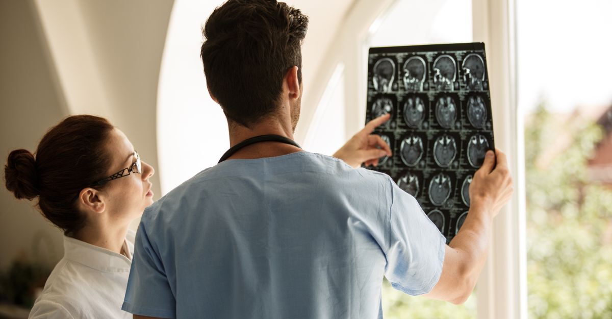 Due medici osservano e analizzano insieme una serie di immagini di risonanza magnetica cerebrale, esaminate alla luce di una finestra.