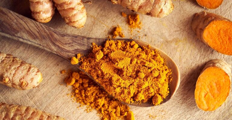 Un primo piano della curcuma macinata su un cucchiaio di legno.