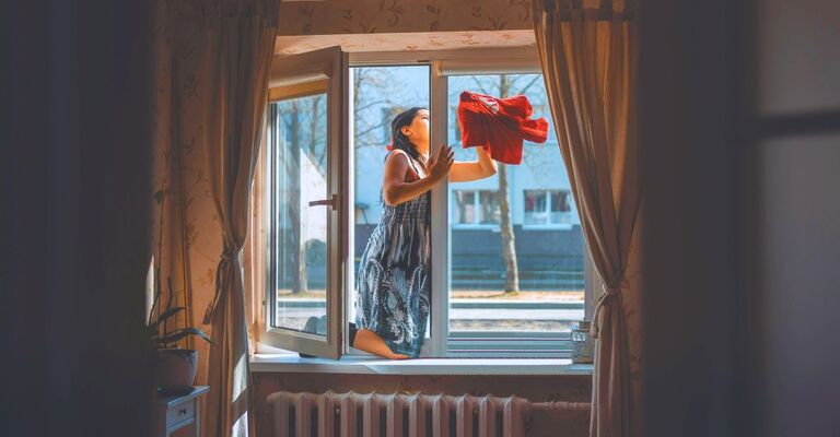 Donna che pulisce i vetri appoggiata al davanzale