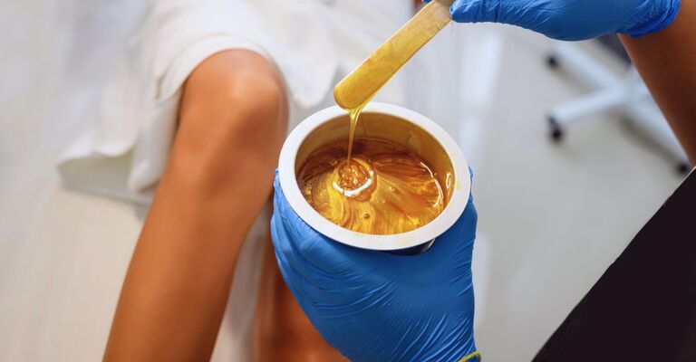 Mani di un'estetista che tengono in mano un barattolo di cera prima di utilizzarla sulle gambe di una cliente