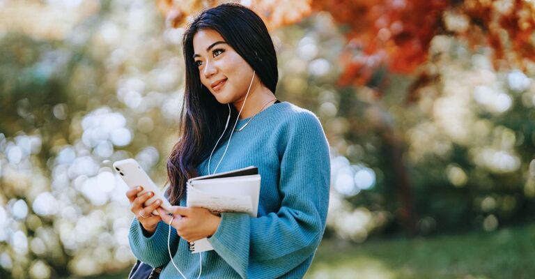 Ragazza con in mano un quaderno e il telefono mentre messaggia e sorride