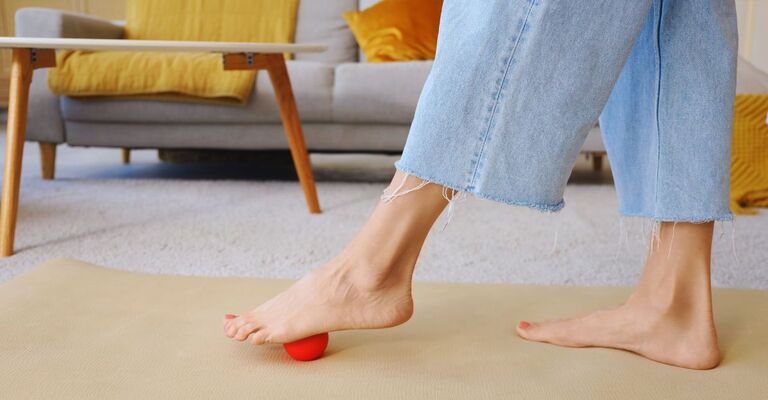 Primo piano di due gambe con un piede che passa sopra a una pallina