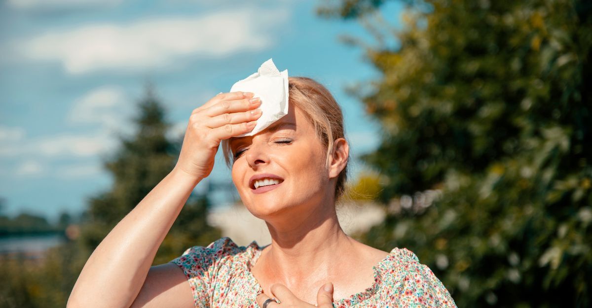Donna di mezza età accaldata si asciuga il sudore con un fazzoletto sotto il sole estivo, simbolo degli effetti del riscaldamento globale sulla salute femminile.
