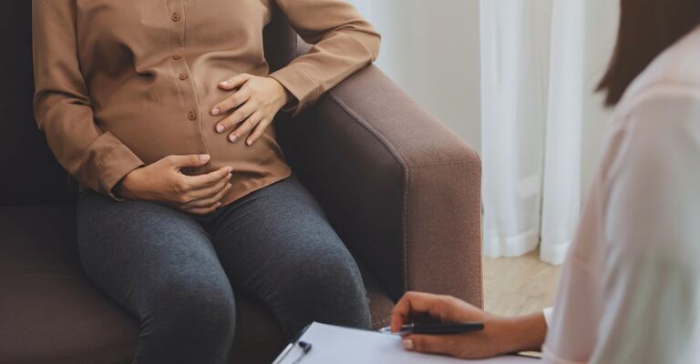 Donna incinta sul divano che viene visitata dalla ginecologa con una cartellina in mano
