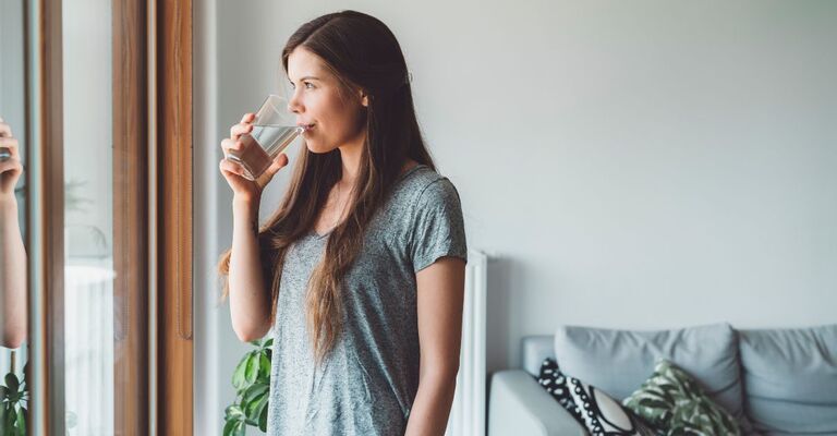Donna che beve da un bicchiere mentre guarda fuori dalla finestra