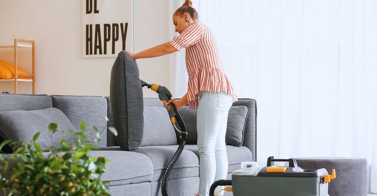 Donna che pulisce il divano con un aspiratore apposito