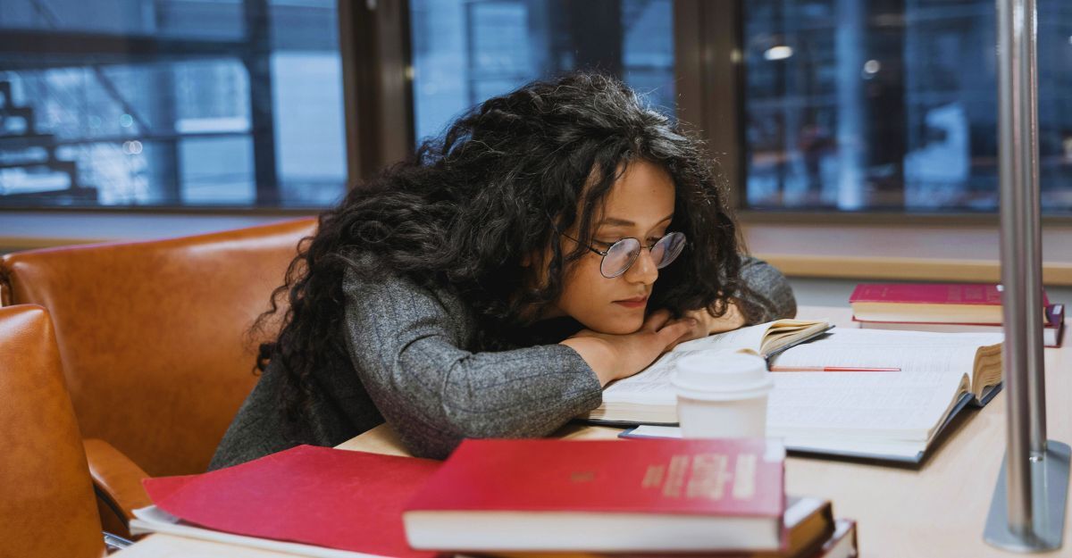Ragazza con la testa sui libri mentre studia in biblioteca