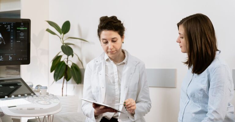Medico con camice bianco mostra e spiega i risultati a una paziente in ambulatorio, accanto a un'ecografo.
