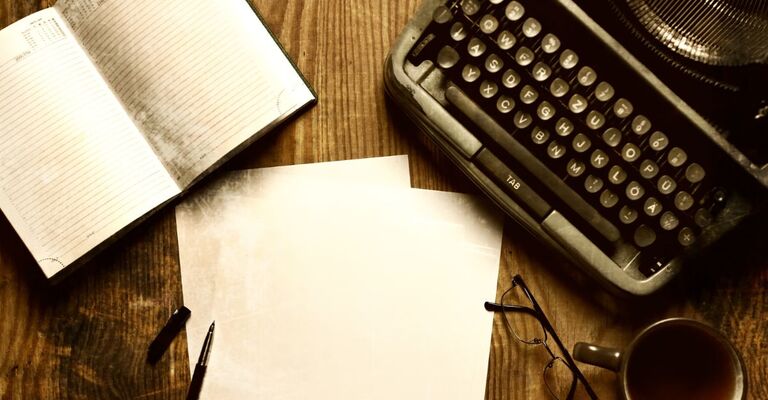 Fogli, tazza di caffè, occhiali e macchina da scrivere su un tavolo