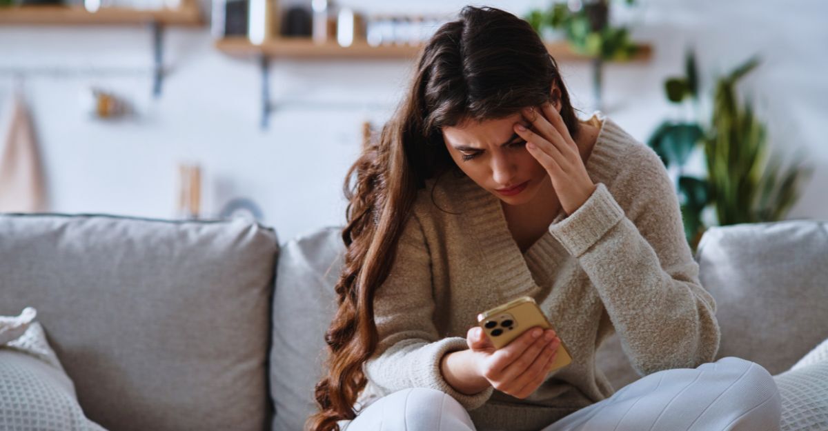Ragazza che scrolla sul cellulare preoccupata mentre è seduta sul divano