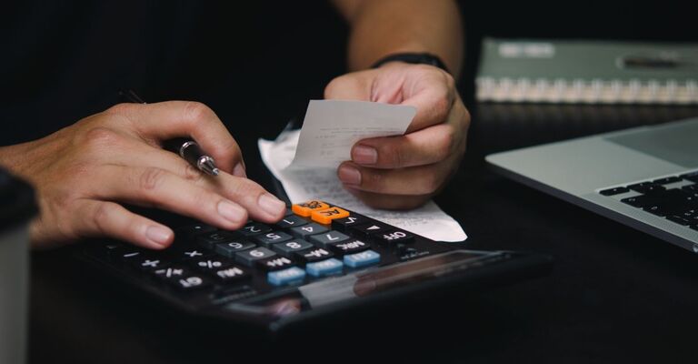 Mani che controllano ricevute e fanno conti con calcolatrice e computer portatile.