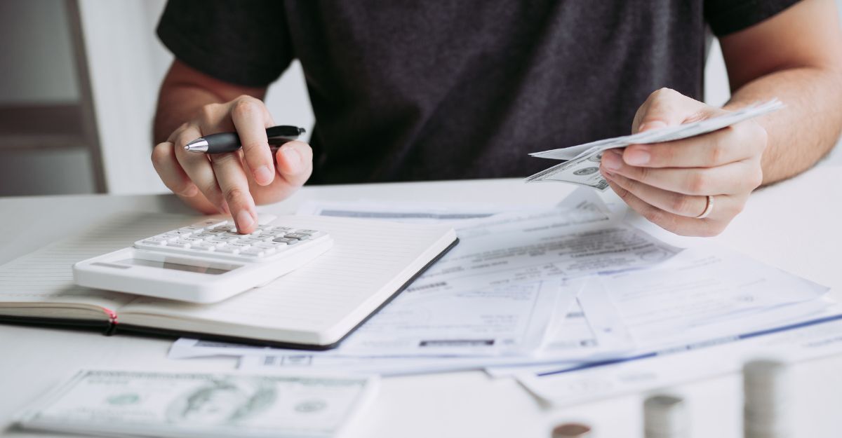 Persona che calcola spese e budget con calcolatrice, banconote e documenti su un tavolo.