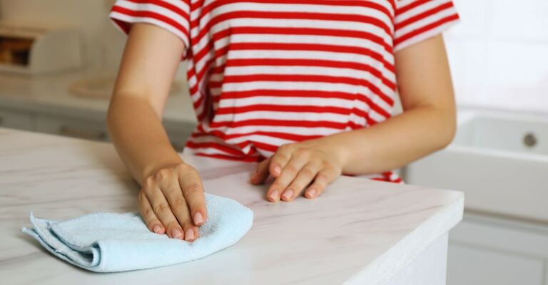Donna con maglietta a righe rosse e bianche che passa un panno in microfibra sul piano della cucina in marmo bianco