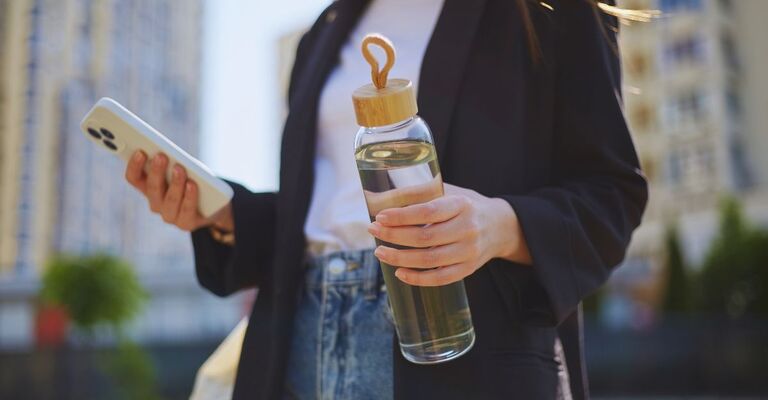 Ragazza in mise da ufficio con in mano lo smartphone e la borraccia
