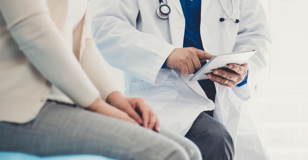 Un medico mostra i risultati degli esami ad una paziente seduta su un lettino di ospedale