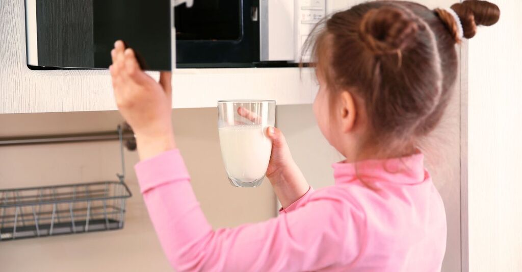 Una bambina sta mettendo un bicchiere di vetro con del latte in un microonde