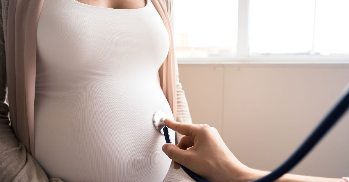 Medico che ausculta con lo stetoscopio la pancia di una donna incinta durante una visita prenatale.