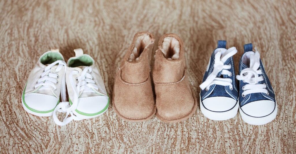 Tre paia di scarpine da neonato di diversi modelli e colori su sfondo in legno chiaro.