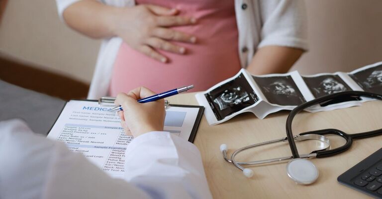 Dottoressa che compila sulla cartellina un foglio con la diagnosi di una paziente incinta che ha fatto un'ecografia